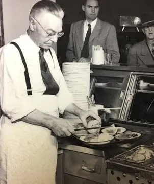 Historic black-and-white photo of Philippe Mathieu preparing sandwiches at Philippe the Original