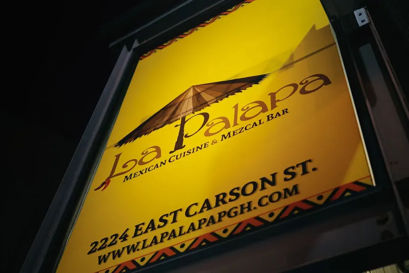 La Palapa's illuminated yellow street sign on East Carson Street, reading "Mexican Cuisine & Mezcal Bar" beneath a palapa-roof logo
