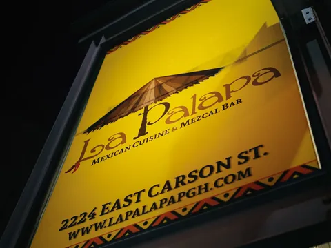 La Palapa's illuminated yellow street sign on East Carson Street, reading "Mexican Cuisine & Mezcal Bar" beneath a palapa-roof logo