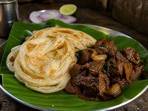 Malabar porotta layered flatbread served with a dark Kerala-style beef curry on a banana leaf at Malabar Kitchen in Richardson