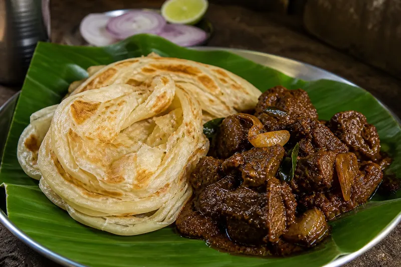 Malabar porotta layered flatbread served with a dark Kerala-style beef curry on a banana leaf at Malabar Kitchen in Richardson