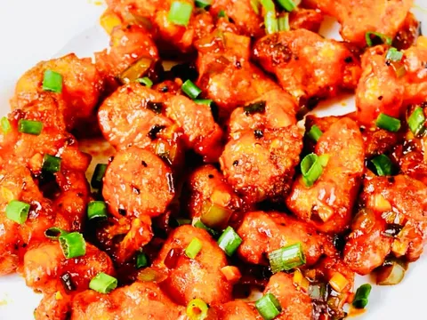 A plate of Rasam's Indo-Chinese style battered chicken tossed in a glossy red chili-garlic sauce and garnished with scallions, on a floral-rimmed plate