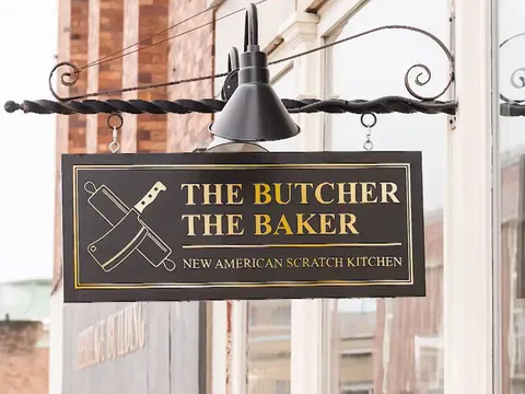 Hanging sign reading The Butcher The Baker, New American Scratch Kitchen, on a brick facade in Bangor