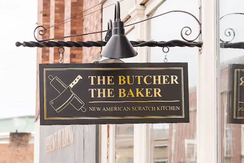 Hanging sign reading The Butcher The Baker, New American Scratch Kitchen, on a brick facade in Bangor