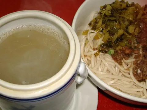 Taiwan Pork Chop House in New York — a lidded ceramic pot of clear herbal soup beside a bowl of dry lo mein topped with pickled mustard greens and minced pork