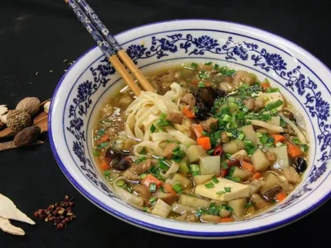 Original Pork Noodles at Shan Xi Magic Kitchen — hand-made noodles in broth with diced tofu, carrot, wood ear and scallion in a blue-and-white porcelain bowl, dried Chinese spices arranged alongside
