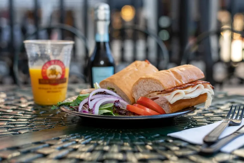 Plated turkey and cheese French bread sandwich with side salad and a Cafe Beignet cup of orange juice at Cafe Beignet