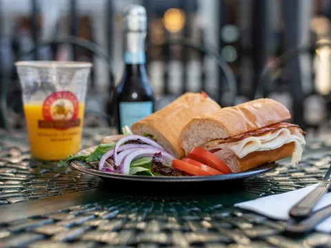 Plated turkey and cheese French bread sandwich with side salad and a Cafe Beignet cup of orange juice at Cafe Beignet