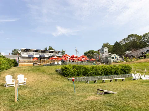 Lawn with Adirondack chairs looking toward the red umbrellas of Island Lobster Company on Peaks Island