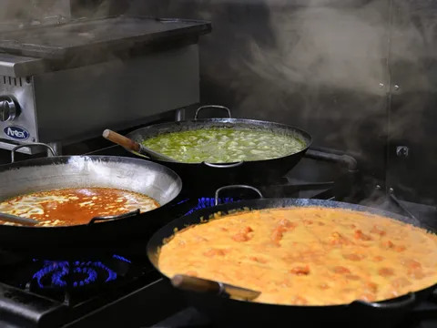 Three steaming karahi pans of curry — green saag, a red masala and an orange butter-chicken-style gravy — cooking on the stove in the kitchen at Masala in Missoula