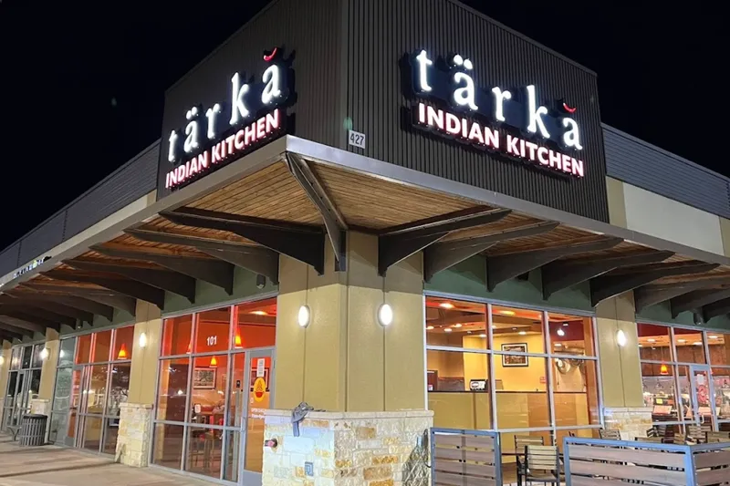 Exterior storefront of Tarka Indian Kitchen at its Stone Oak location in San Antonio at night, with the illuminated tarka Indian Kitchen sign above the entrance