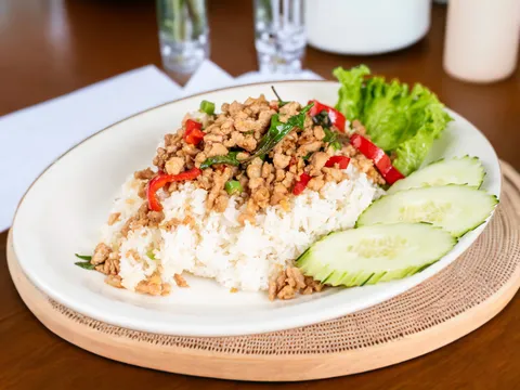 Thai basil chicken with red chilis over jasmine rice with cucumber and lettuce on a white plate at Lers Ros Thai