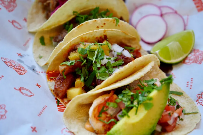 Three tacos with cilantro, onion, pineapple, avocado and shrimp on Taqueria Habanero branded paper, with lime and radish, at Taqueria Habanero in Washington, DC