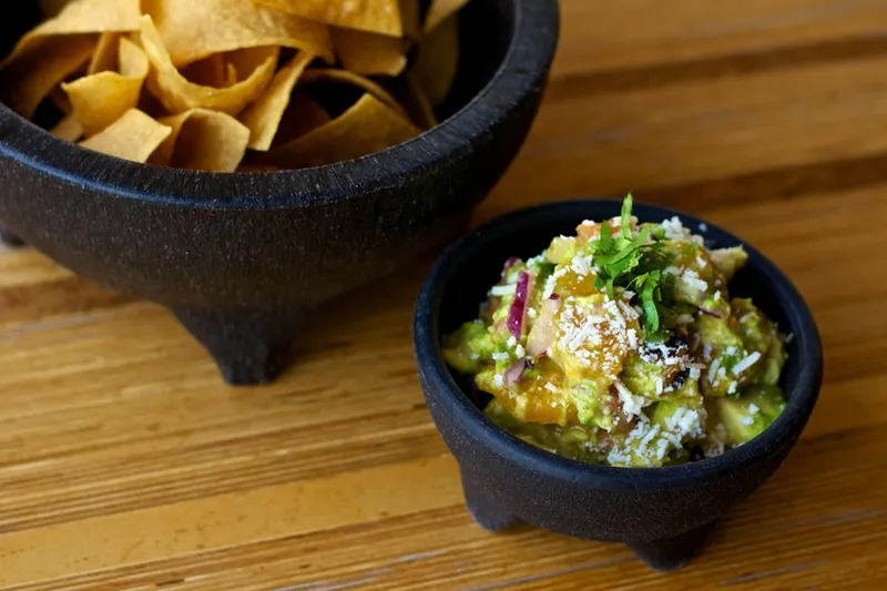 Gallo guacamole topped with cotija and cilantro in a stone molcajete beside a bowl of tortilla chips at Gallo Blanco