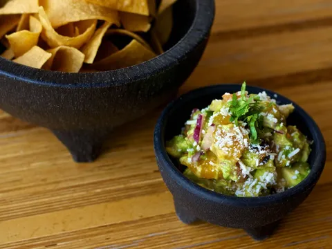 Gallo guacamole topped with cotija and cilantro in a stone molcajete beside a bowl of tortilla chips at Gallo Blanco
