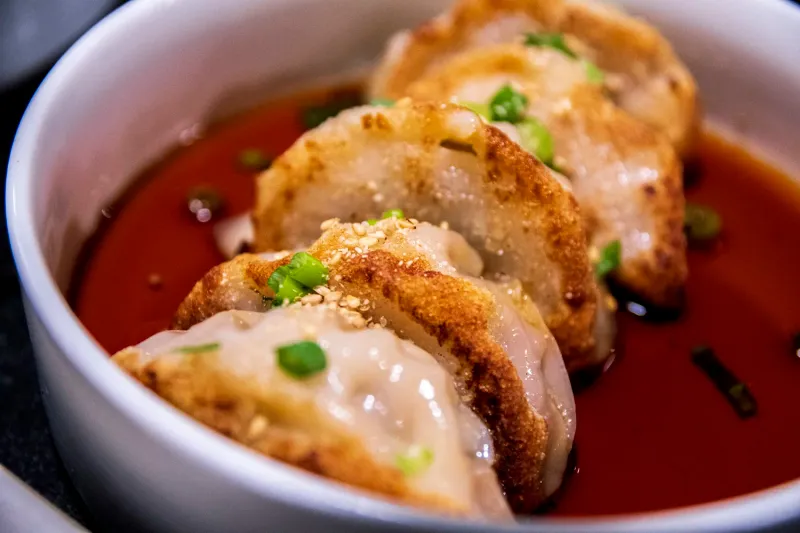 Pan-fried pork and kimchi mandu dumplings in chili sauce topped with scallions and sesame at Anju