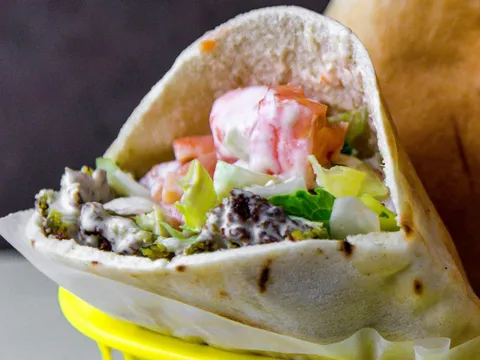 A falafel pita sandwich with lettuce, tomatoes and tahini in a basket at Mamoun's Falafel