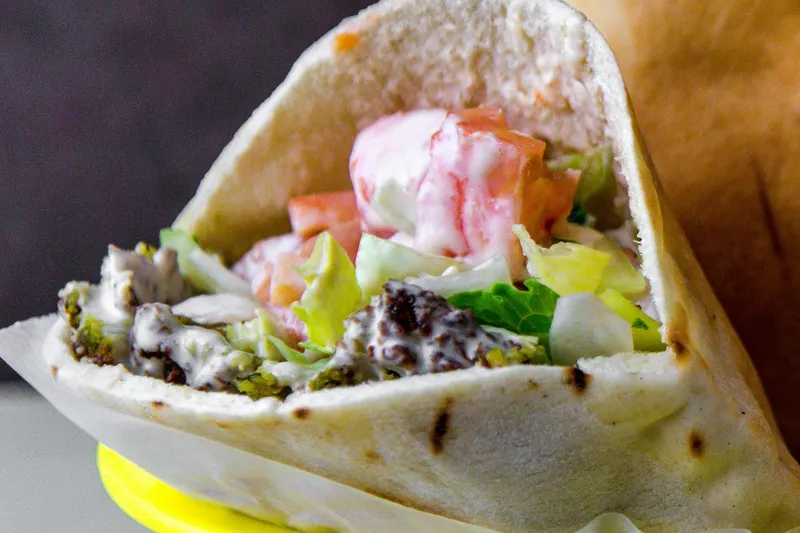 A falafel pita sandwich with lettuce, tomatoes and tahini in a basket at Mamoun's Falafel