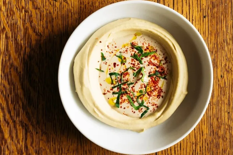 Bowl of classic tahini hummus topped with olive oil, Aleppo pepper and herbs at Saba in New Orleans
