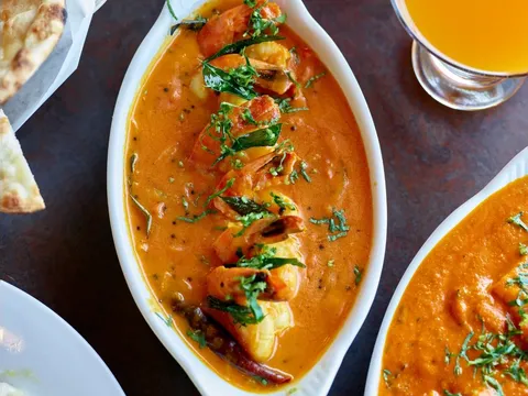 Kerala shrimp curry in a white dish at Cardamom, with naan, mango lassi and butter chicken alongside