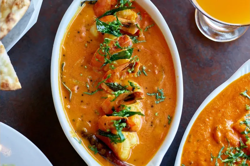 Kerala shrimp curry in a white dish at Cardamom, with naan, mango lassi and butter chicken alongside