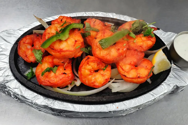 Tandoori shrimp on a foil-lined sizzler platter with sliced onions, lemon and a cup of mint chutney at Taste of Chennai in Hicksville