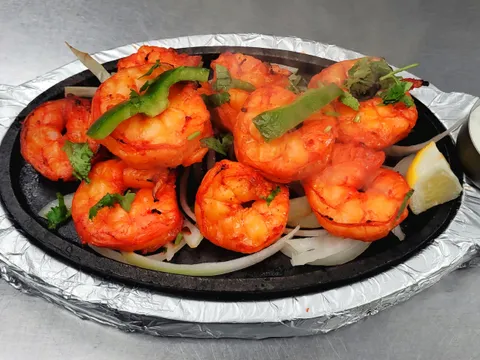 Tandoori shrimp on a foil-lined sizzler platter with sliced onions, lemon and a cup of mint chutney at Taste of Chennai in Hicksville