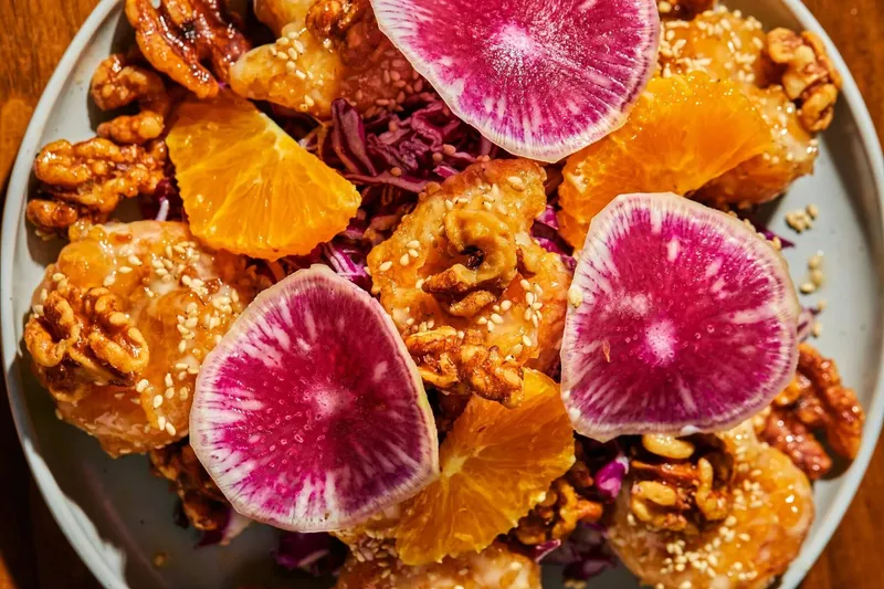 Walnut shrimp with orange slices, red cabbage, candied walnuts, sesame seeds, and watermelon radish slices