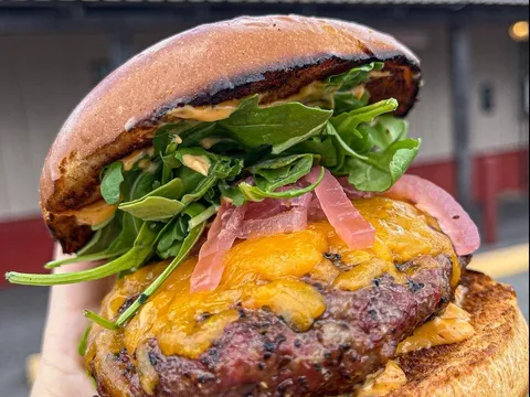 Cheeseburger held up in front of the Pizzitola's sign