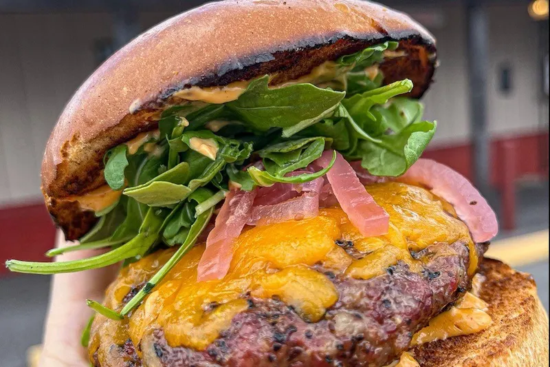 Cheeseburger held up in front of the Pizzitola's sign