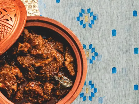 Kosha mangsho-style goat curry served in a lidded terracotta clay pot on a blue-and-gold jamdani-patterned cloth at Korai Kitchen in Jersey City