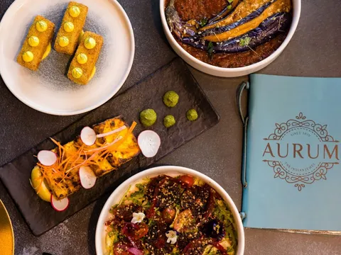 A spread of Aurum's modern Indian dishes — paneer tikka, kofta, eggplant curry and a chaat bowl — beside the branded Aurum menu booklet