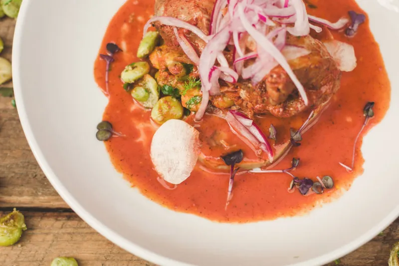 A Yucatecan entrée in a bright red achiote-tomato sauce topped with pickled red onions and lima beans, plated on a white bowl at The Mayan Cafe in Louisville