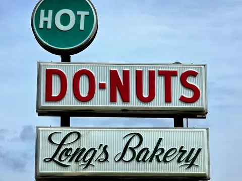 "Hot Do-Nuts, Long's Bakery" sign against a blue sky