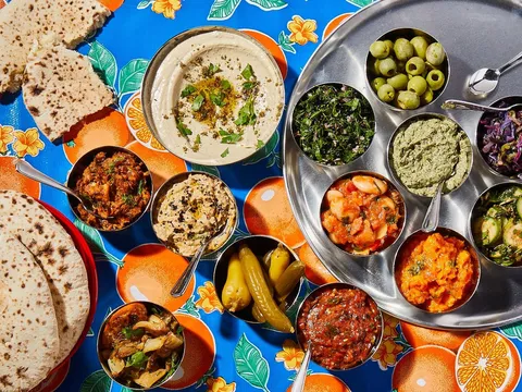 Overhead spread of Laser Wolf salatim - hummus, olives, dips and pita on a colorful tablecloth
