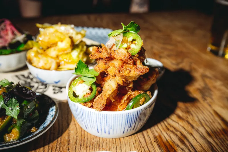 Bowl of salt-and-pepper fried squid with sliced jalapeno and cilantro, among shared dishes on a wood table, at Four Kings in San Francisco Chinatown