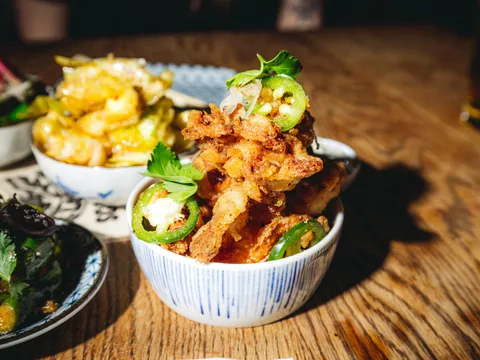 Bowl of salt-and-pepper fried squid with sliced jalapeno and cilantro, among shared dishes on a wood table, at Four Kings in San Francisco Chinatown
