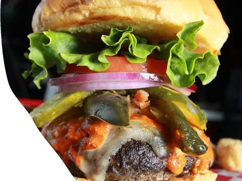 Close-up of a loaded cheeseburger with jalapenos, lettuce and tomato at The Vortex Bar & Grill