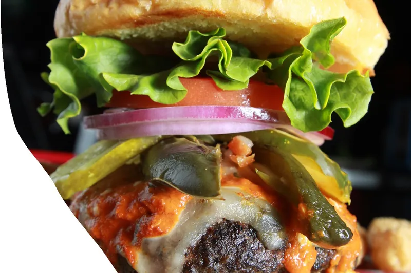 Close-up of a loaded cheeseburger with jalapenos, lettuce and tomato at The Vortex Bar & Grill