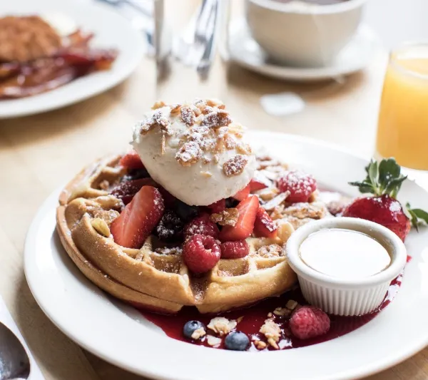 Clinton St. Baking Company buttermilk waffle topped with fresh berries, whipped cream and toasted nuts with maple butter and coffee