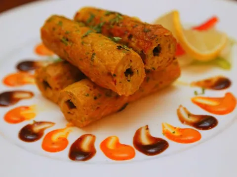 Plated cylindrical kababs garnished with cilantro, served with a lemon wedge and orange and tamarind chutney dots on a white plate, from Mantra in Jersey City, New Jersey