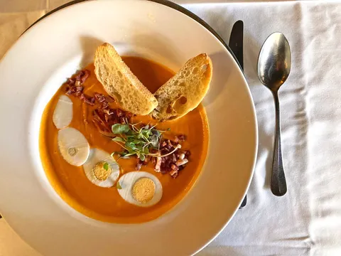 A chilled tomato soup (salmorejo) garnished with microgreens, chopped chorizo and toasted bread on a white-clothed table at Madeira Restaurant