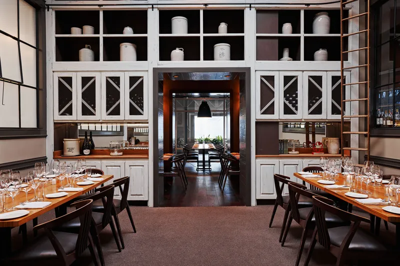 Miller Union dining room with set wooden tables, wine glasses and floor-to-ceiling white shelving lined with stoneware crocks
