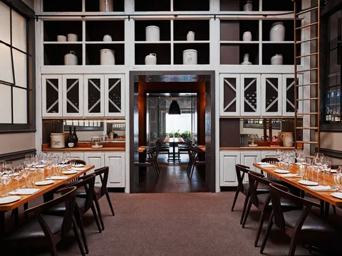 Miller Union dining room with set wooden tables, wine glasses and floor-to-ceiling white shelving lined with stoneware crocks