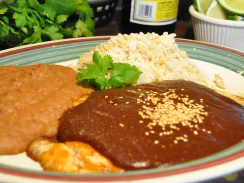Mole poblano con pollo — chicken breast under dark poblano mole sauce topped with sesame seeds, with Mexican rice and refried beans at Guajillo's