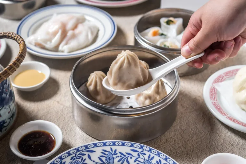 A steamed soup dumpling lifted with a spoon from a bamboo steamer basket at Nom Wah Tea Parlor