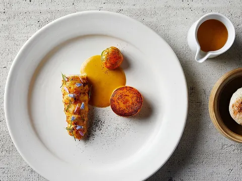 Overhead view of an artfully plated Indienne course with sauce and a crisp spiral garnish