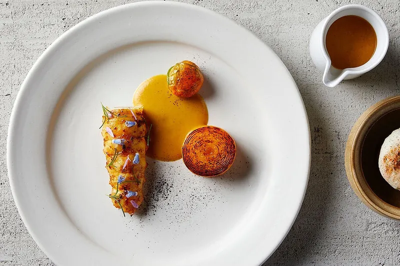 Overhead view of an artfully plated Indienne course with sauce and a crisp spiral garnish