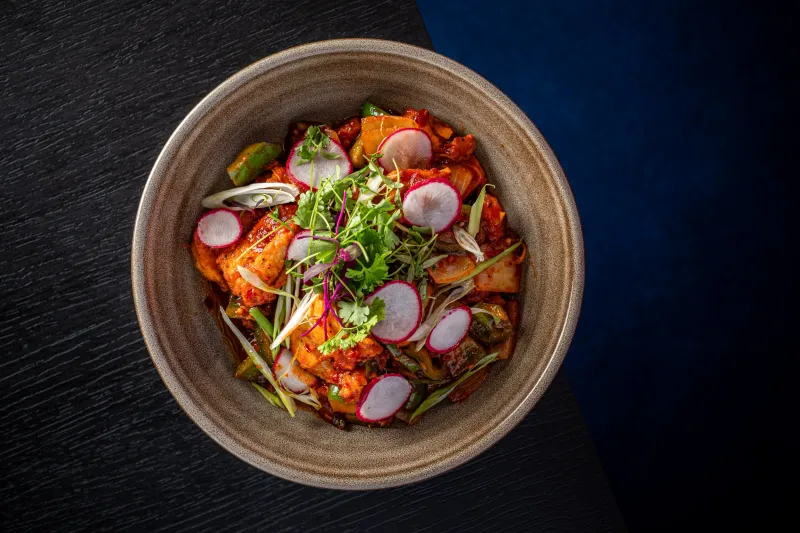 Bowl of chicken chilli garnished with radish, scallion and cilantro at Vajra