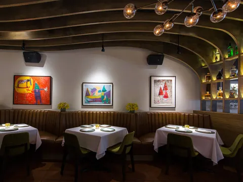 Topolobampo dining room with brown leather banquette, white-clothed tables, green chairs and framed Mexican folk art